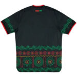 Back view of a black shirt with green zigzag trim on the sleeves and a geometric teal and red pattern along the hem across the bottom edge.