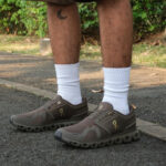 408a1ccc-bfff-416f-adc2-a1dde64e4c26 | UAE SPORT STORE Lower legs wearing brown athletic shoes with white socks, standing on a paved path; crescent tattoo on the left leg visible.