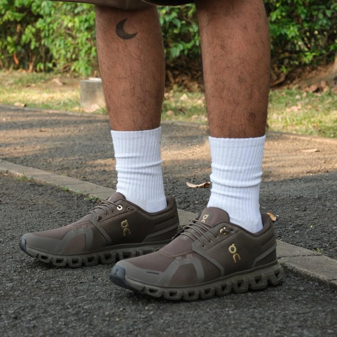 408a1ccc-bfff-416f-adc2-a1dde64e4c26 | UAE SPORT STORE Lower legs wearing brown athletic shoes with white socks, standing on a paved path; crescent tattoo on the left leg visible.