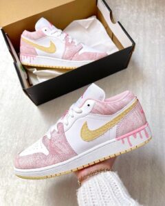 Pastel pink and white Nike sneakers with a gold swoosh, shown outside and inside their open shoe box.