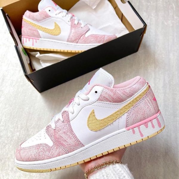 Pastel pink and white Nike sneakers with a gold swoosh, shown outside and inside their open shoe box.