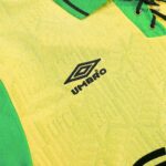 Close-up of a yellow soccer jersey with green sleeves and the black Umbro logo.
