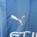 Close-up of blue knit fabric with a large white curved graphic partially visible, likely part of a logo or text.
