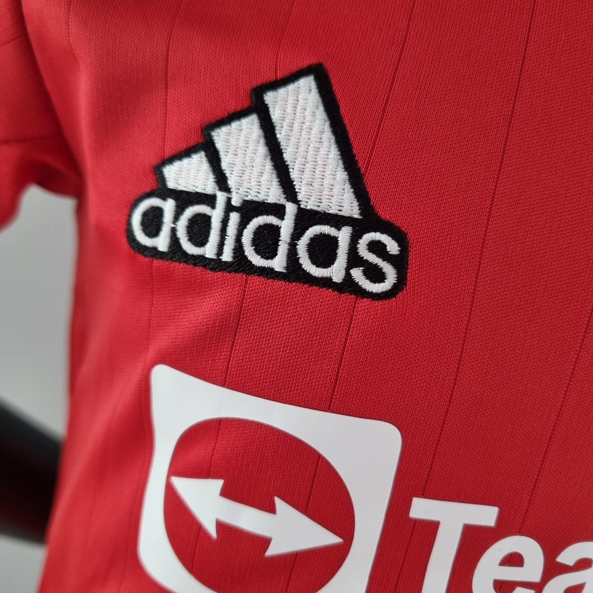 419d2a0b_ce678b67-f536-47d2-88fe-6783fbb201e9 | UAE SPORT STORE Close-up of a red sports jersey with an embroidered white Adidas logo patch partially visible.