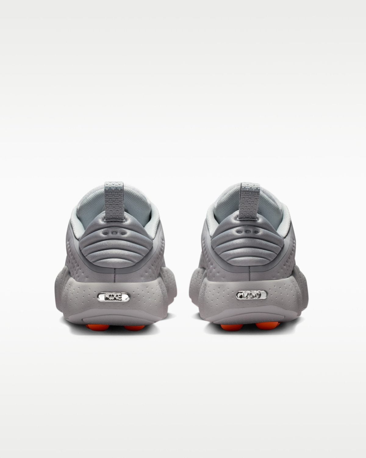 Pair of gray sneakers shown from the back, featuring textured straps and orange outsole accents.