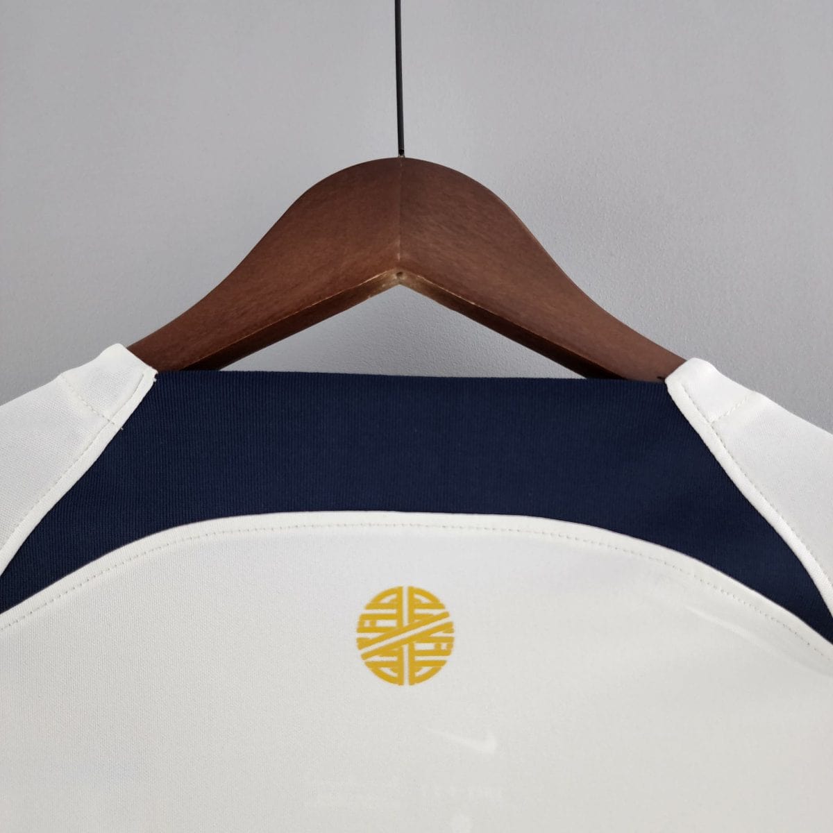Wooden clothes hanger holding a navy garment with white stitching; a small yellow circular logo is visible on the fabric.