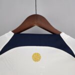 Wooden clothes hanger holding a navy garment with white stitching; a small yellow circular logo is visible on the fabric.