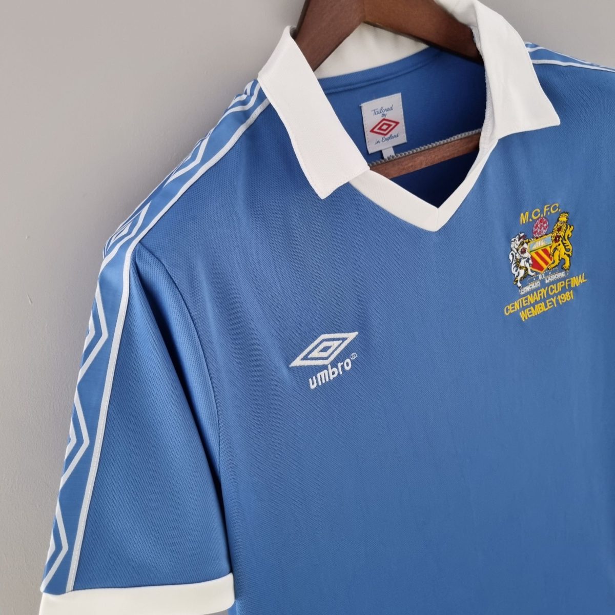 Blue soccer jersey on a wooden hanger with a white collar, displaying the club crest on the chest.