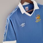 4205857a_88d101fe-eb49-48c2-9bd2-3ad5fa677d81 | UAE SPORT STORE Blue soccer jersey on a wooden hanger with a white collar, displaying the club crest on the chest.
