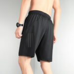 Back view of a man wearing black athletic shorts with an elastic waistband and subtle vertical stripes on the side.