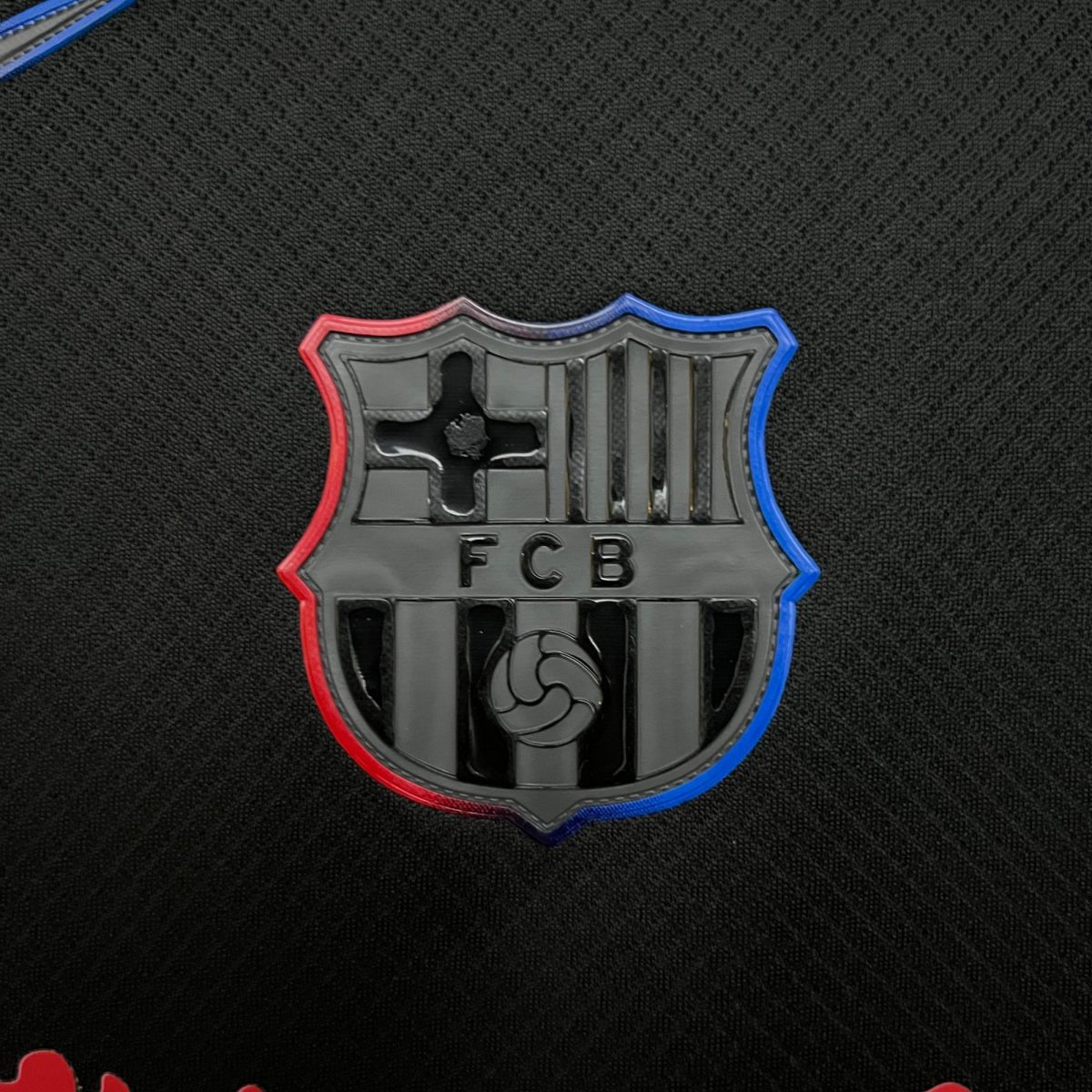 Close-up of a shield-shaped sports badge with red and blue edges on a black textured surface.