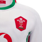 White rugby jersey featuring the Welsh Rugby Union (WRU) crest in red on the chest with green collar trim and side accents.