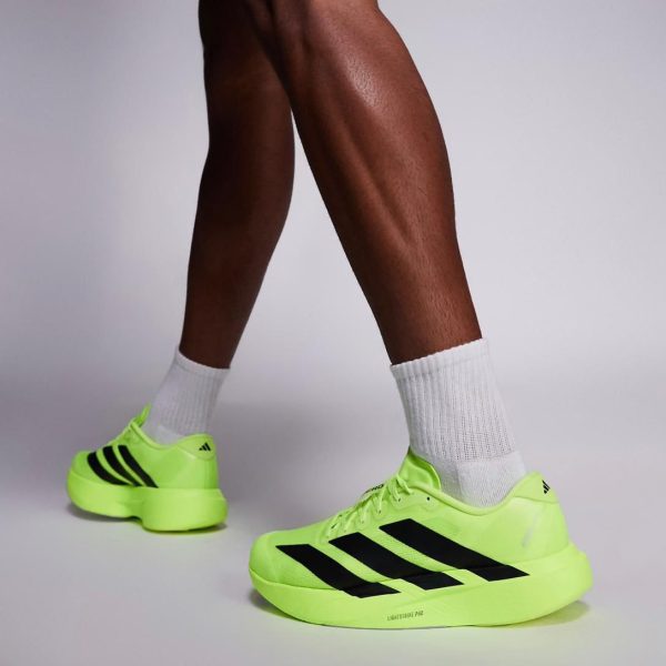 Neon yellow-green Adidas running shoes with black stripes on white socks, close-up of feet in a studio setting.