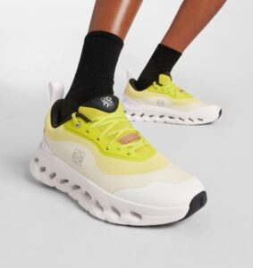 43af550d-c302-46e9-885d-447d33f92e7d | UAE SPORT STORE Bright yellow chunky sneakers with white thick sole on a model wearing black socks, close-up view of one foot in front of the other on a gray background