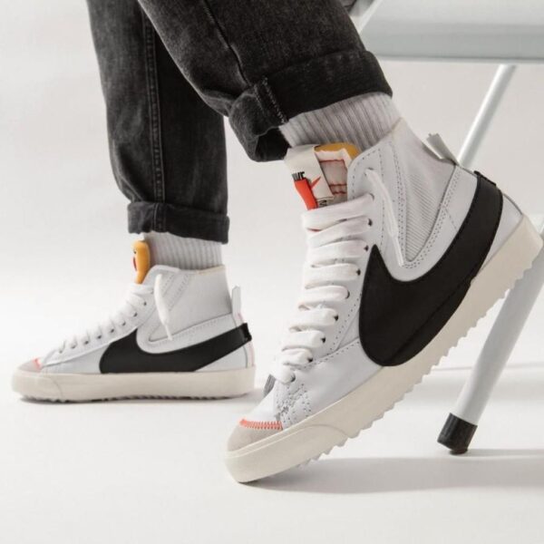 White high-top sneakers with a black side panel, worn with cuffed jeans in a bright studio setting.