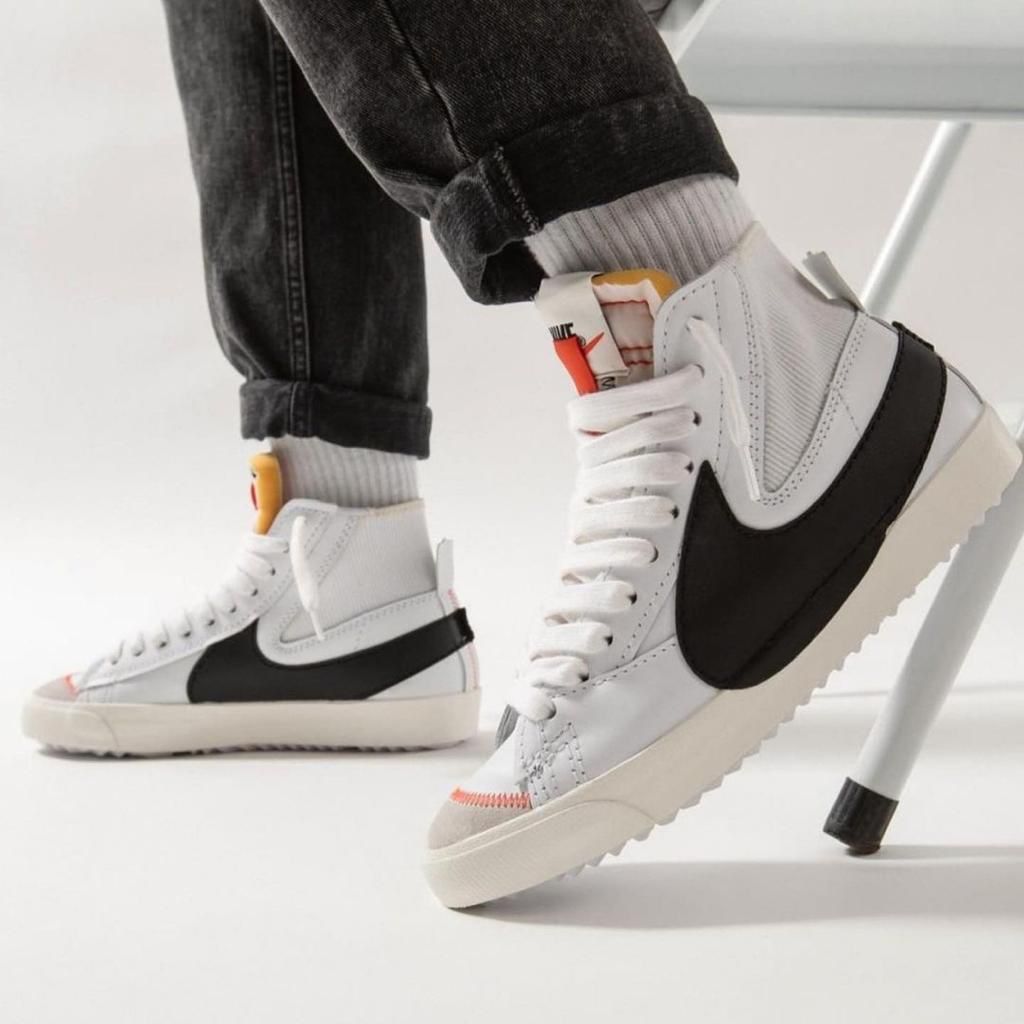43c61a0b-1ec8-4d79-abd0-3f986b618ad1 White high-top sneakers with a black side panel, worn with cuffed jeans in a bright studio setting.