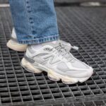 Close-up of a light gray chunky sneaker stepping on a metal grate, with blue jeans visible at the ankle edge.