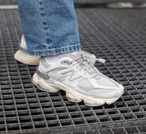 Close-up of a light gray chunky sneaker stepping on a metal grate, with blue jeans visible at the ankle edge.