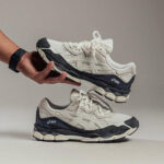 Pair of white and navy ASICS running shoes, one held above the other by a hand.