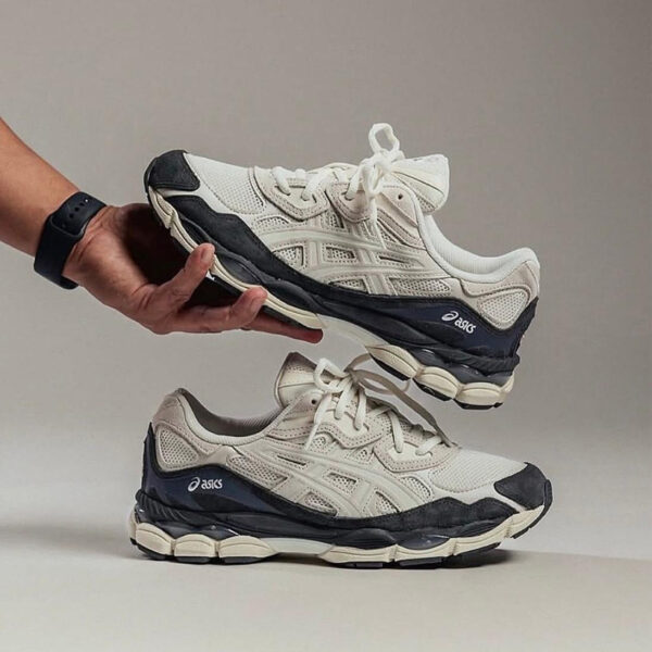 Pair of white and navy ASICS running shoes, one held above the other by a hand.
