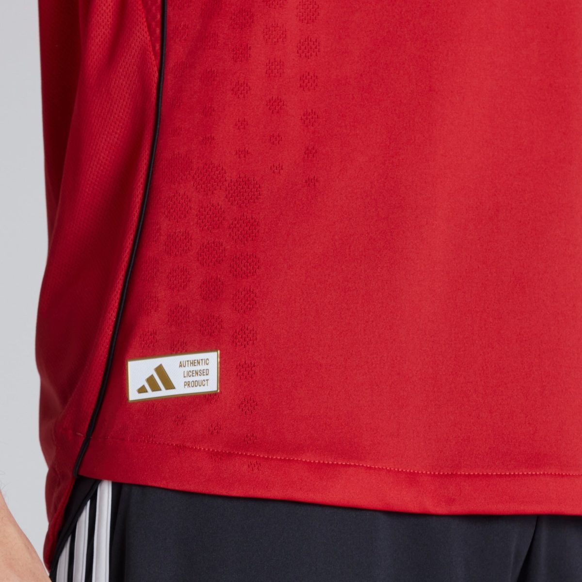 Close-up of red sports jersey fabric with a dotted pattern and an Adidas authentic licensed product patch.