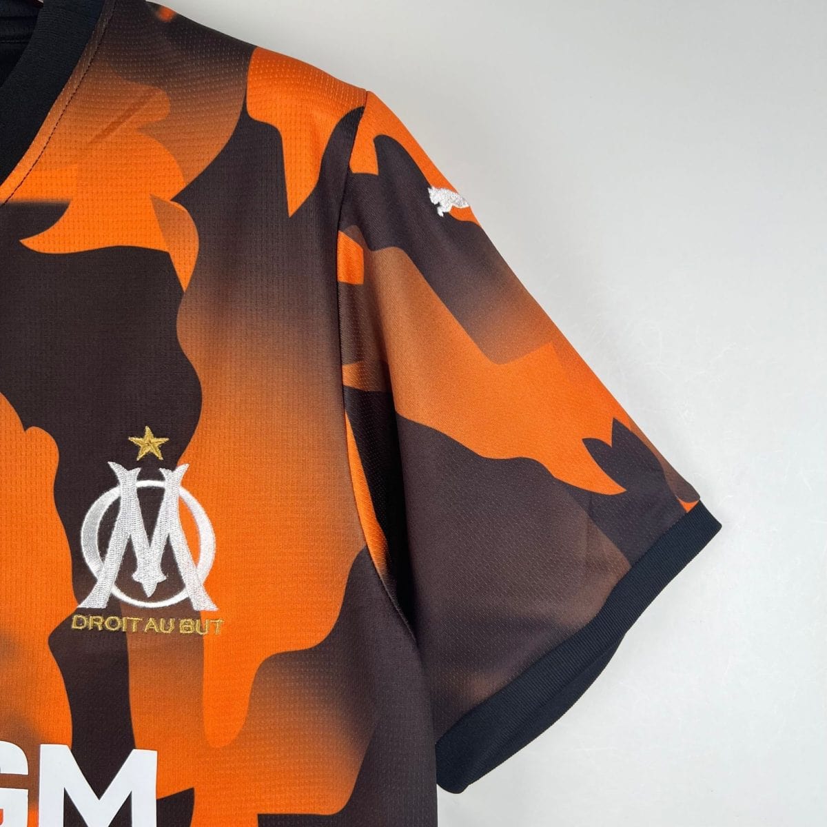 Close-up of an orange and black camouflage jersey sleeve, showing a white circular emblem and small stars partially visible near the cuff.