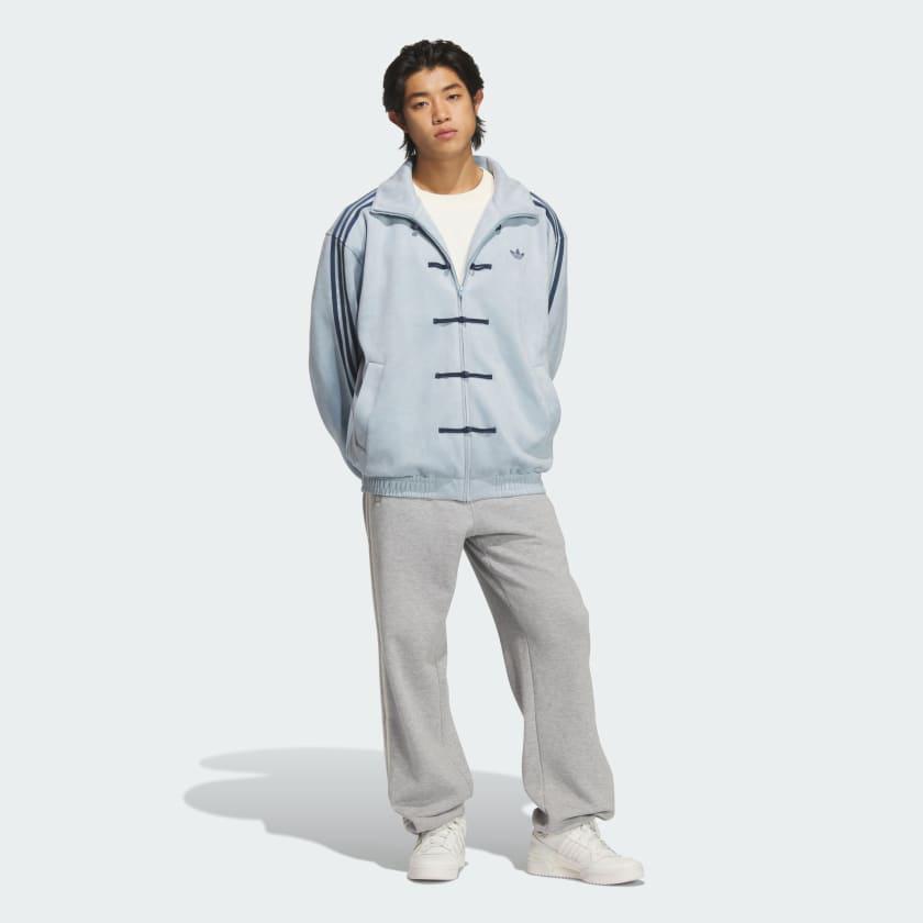44a767f4-8bb0-443b-95f9-5137a56a309d | UAE SPORT STORE Young man wearing a light blue zip-front jacket with toggle closures, paired with gray sweatpants and white sneakers.