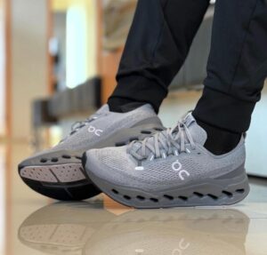 44a8b4a6-a5a8-46cf-bcbb-6fadec08f46a | UAE SPORT STORE Gray On running shoes with perforated mesh, laces tied, worn by someone in black pants standing on a glossy floor.