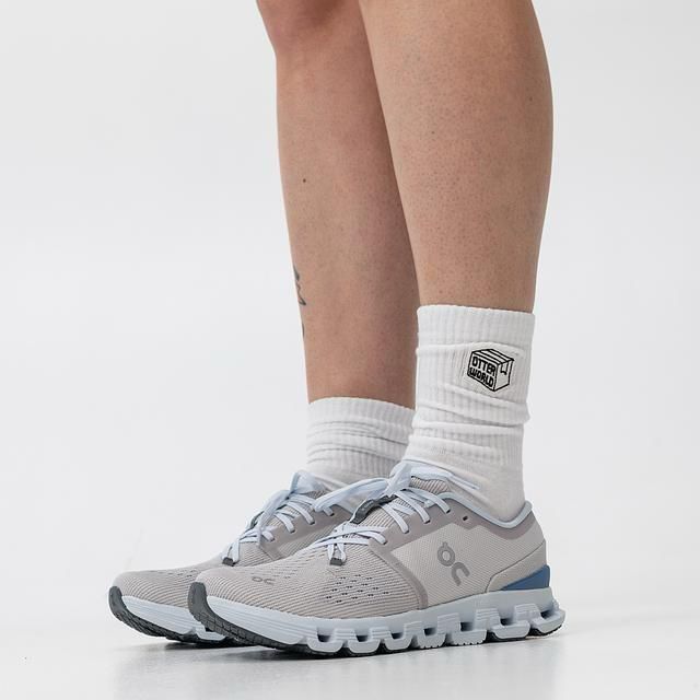 44e1b6fa-36d0-4e84-ad62-0b86b8f2eb8b | UAE SPORT STORE Lower legs wearing white crew socks with a logo patch, paired with light gray athletic sneakers and a chunky sole.