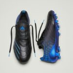 453e9770-3ac7-4fa7-9555-b2becb463af3 | UAE SPORT STORE Pair of soccer cleats: black shoe with blue accents on the left and a blue-and-black studded shoe on the right, laces untied.