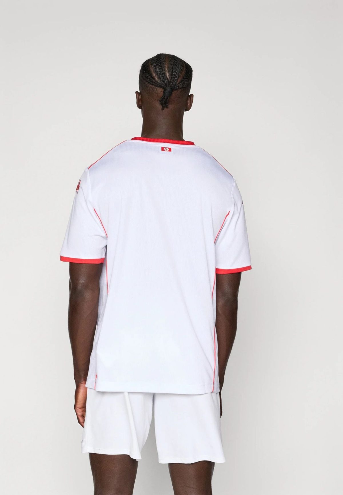 Back view of a person wearing a white athletic jersey with red trim, small flag patch on the upper back.