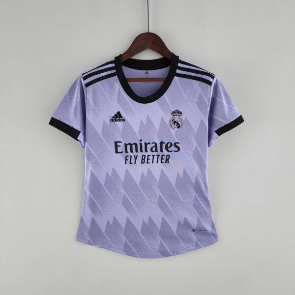 Light purple Real Madrid jersey on a wooden hanger against a pale wall, displaying Emirates Fly Better text and Adidas logos.
