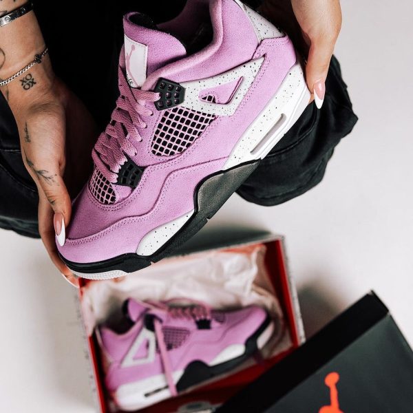 Close-up of a pink and white Air Jordan sneaker being held, with another pink pair inside a red Jordan box nearby.