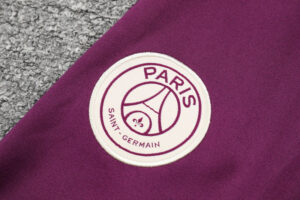 Circular Paris Saint-Germain emblem patch on purple fabric, featuring a white background and fleur-de-lis detail.
