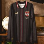 Black pinstripe soccer jersey with red center stripe, Puma logo, and a crest on the chest, hanging on a hanger.