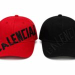 Red and black Balenciaga baseball caps with diagonal black lettering across the crown, shown side by side.