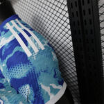 Close-up of a blue patterned athletic jersey sleeve with white Adidas stripes next to a chain-link fence.