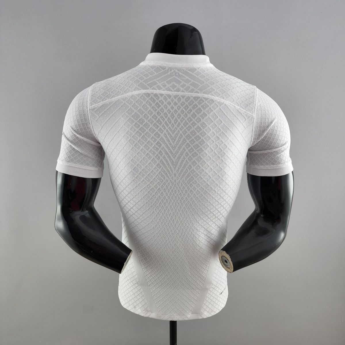 Back view of a white textured knit top on a black mannequin bust against a gray background, clothing display image.