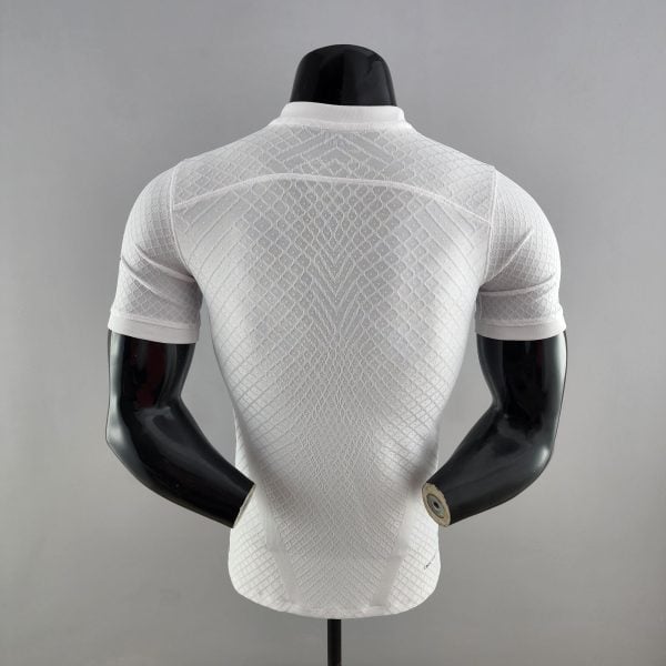 Back view of a white textured knit top on a black mannequin bust against a gray background, clothing display image.