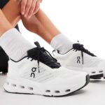 Person tying the laces of white athletic sneakers with black accents and gray socks