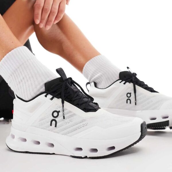 Person tying the laces of white athletic sneakers with black accents and gray socks