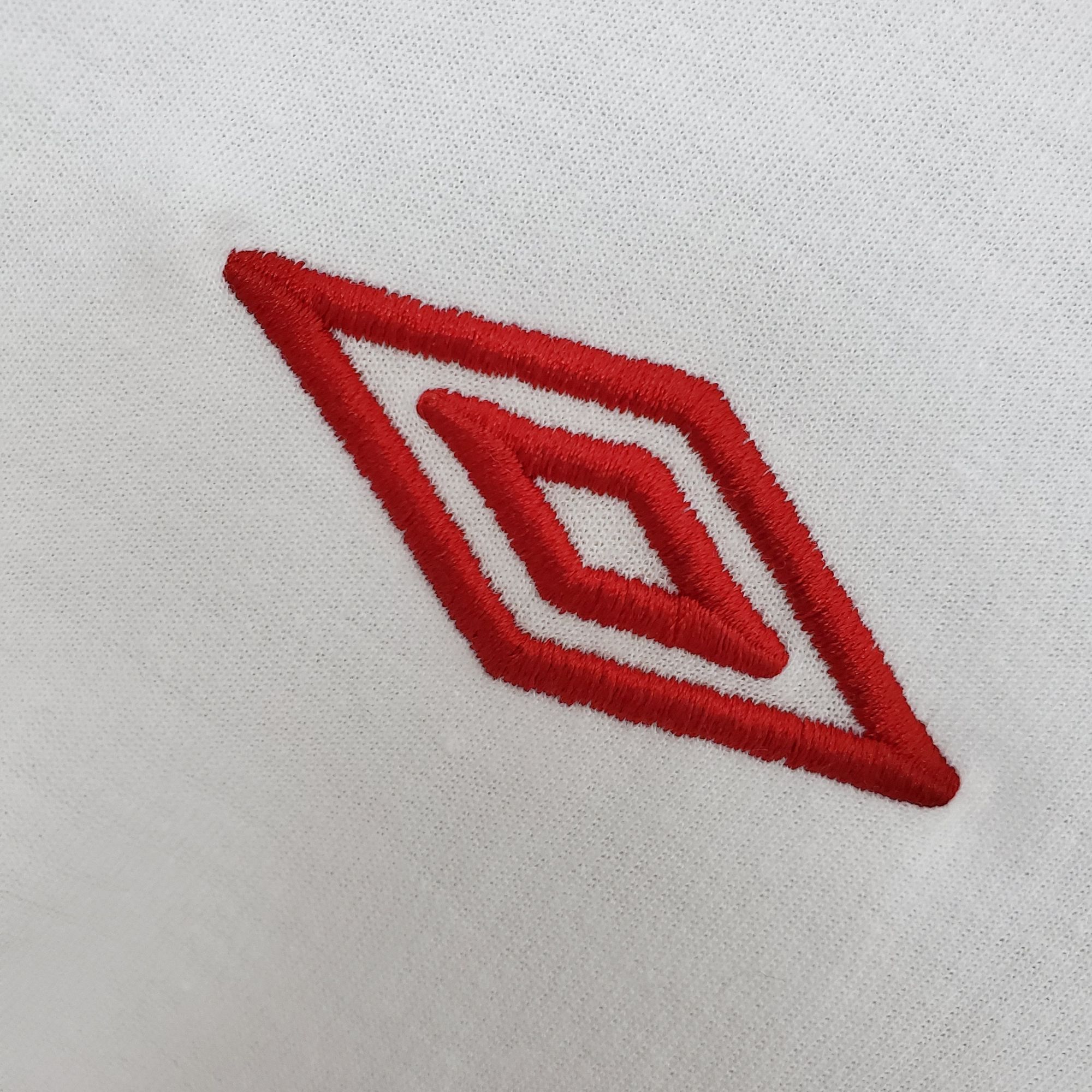 47175d94_1_1d9fd32b-8e92-406e-a677-c016546678df | UAE SPORT STORE Close-up of white textured fabric with red embroidered curved lines visible in the lower left corner.