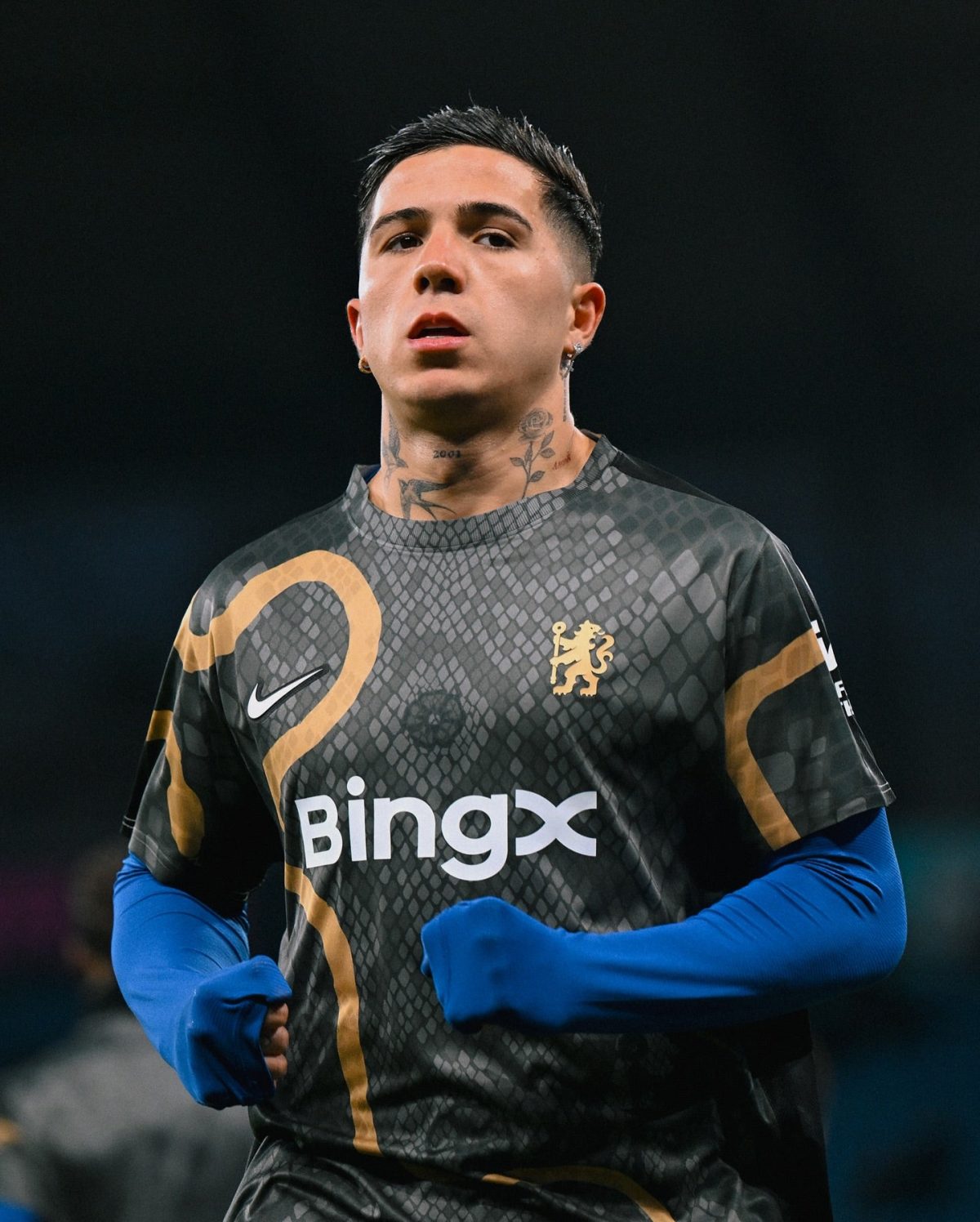 Soccer player in a dark geometric-pattern jersey with gold crest, blue sleeves, and BingX logo, focused expression.