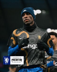 474967389_18492982939021107_5021297882757087593_n | UAE SPORT STORE Athlete in a black patterned jersey with gold accents, blue beanie, and black gloves during warm-up under stadium lights.