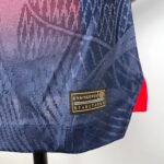 Close-up of dark blue textured fabric with a yellow 'ENGINEERED' tag and red strap visible on the right side.