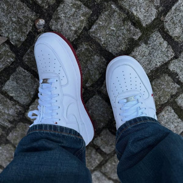 Person wearing white sneakers with red soles standing on rough cobblestone ground, jeans cuffs visible.