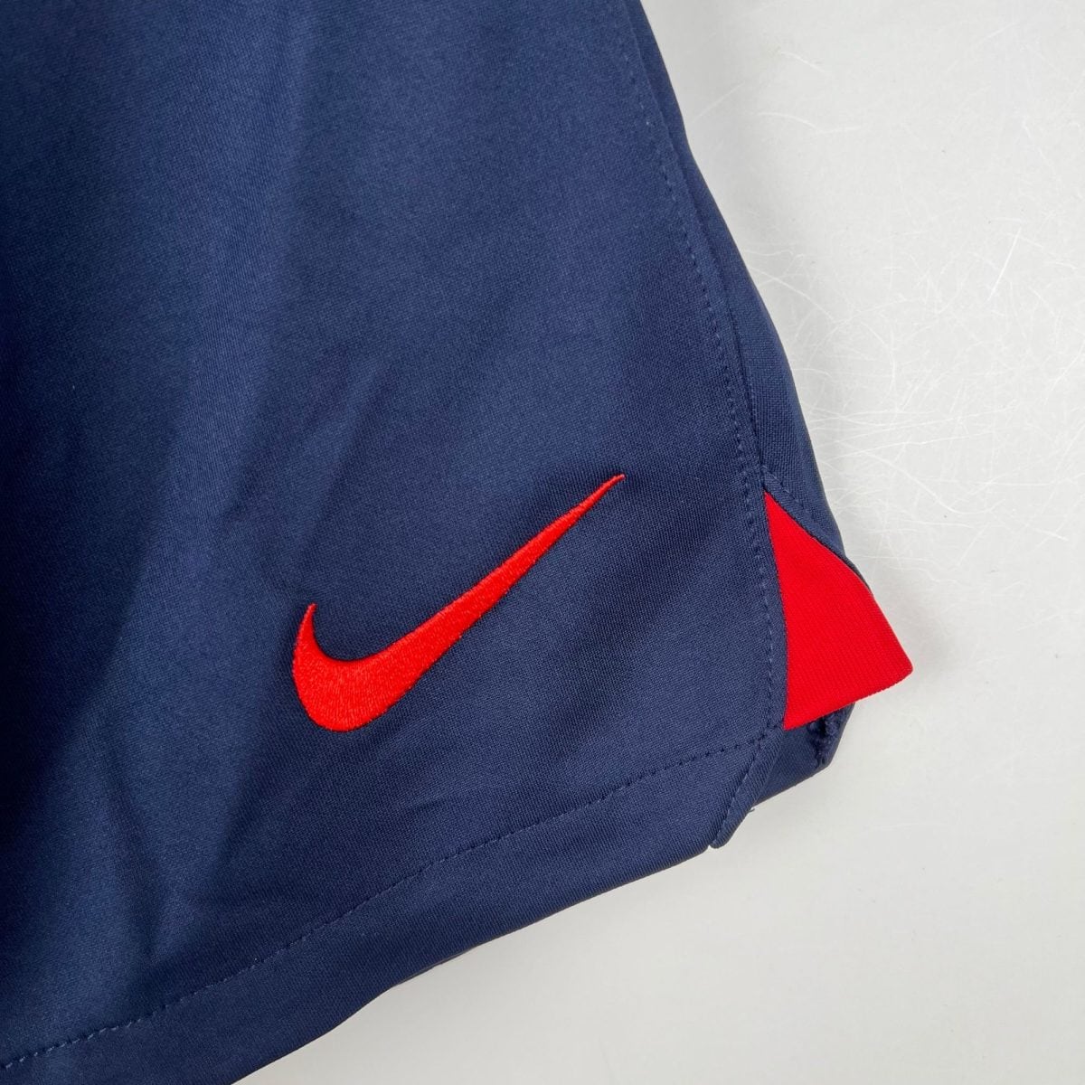 Close-up of dark blue fabric with a red Nike swoosh stitched along a seam nearby.