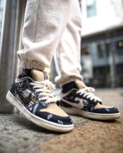 Close-up of stylish sneakers with bandana-patterned navy panels and tan toe, laced, worn with light joggers in an urban setting.