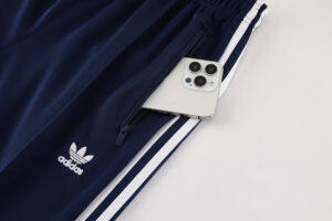 Navy Adidas track pants with white stripes and a zipper pocket holding a smartphone partially visible in the pocket center-right