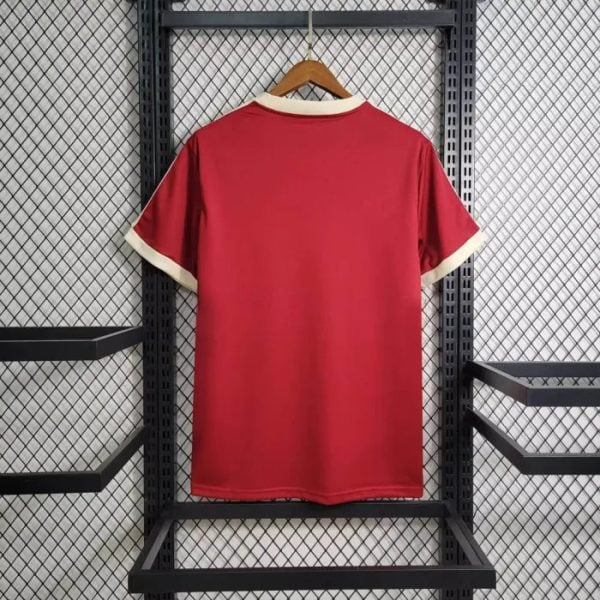 Red short-sleeve sports jersey hanging on a wooden hanger against a metal rack, back view with cream collar and cuffs.